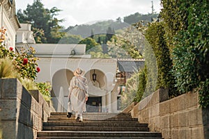 Woman on the stairs in the park. A middle-aged lady in a hat in a white outfit with a bag walks around the Livadia