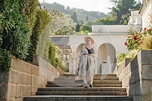 Woman on the stairs in the park. A middle-aged lady in a hat in a white outfit with a bag walks around the Livadia