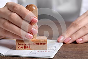 Woman stamping document at wooden table, closeup. Permanent residency visa in Canada