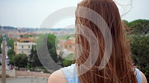 Woman stand on observation deck look at city panorama. Girl`s hair fluttering in wind in slow motion