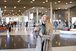 Woman standing in airport hall with valise and neck pillow.