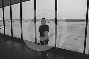 Woman standing in the airport terminal and looking at airplanes while waiting at boarding gate.