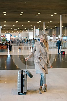 Woman standing in airport waiting room with valise and wearing g