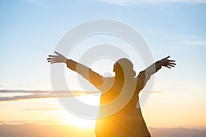 Woman standing alone with arms raised up during beautiful sunrise at the morning.