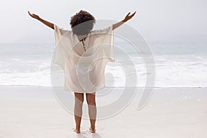 Woman standing with arms outstretched on beach in the sunshine