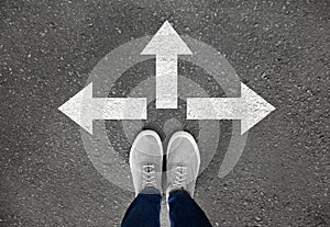 Woman standing on asphalt road with arrows pointing in different directions. Concept of choice photo