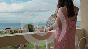 Woman Is Standing On The Balcony, Looking Into Distance At Sea And Passing Ships. Concept Of Relaxation And Waiting For