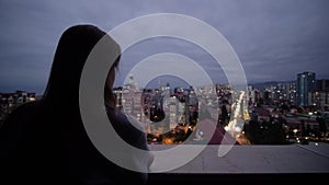 Woman is standing on the balcony and looking at the evening sky over the city