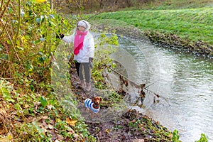 Woman standing on banks of Geleenbeek stream with her dachshund