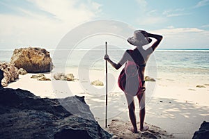 Woman standing on the beach with hat, stick and backpack