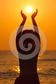 Woman standing on beach, holding sun in hands