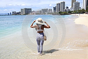 A woman standing  on the beach wearing straw hat and leopard pants