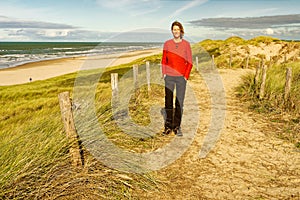 A woman standing on a beautiful sandy trail along the ocean, looking into the camera. North Holland dune reserve, Egmond aan Zee,