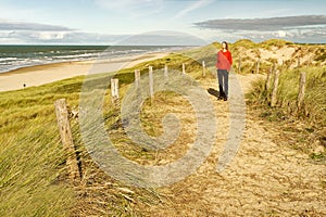 A woman standing on a beautiful sandy trail by the ocean, enjoying the sun. North Holland dune reserve, Egmond aan Zee,