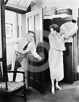 Woman standing behind a door trying to hit a man with a pillow