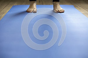 Woman standing on blue yoga mat. Feet with pink pedicure, low perspective
