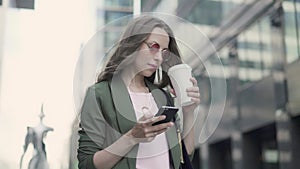 Woman standing in blurred city street web surfing and drinking coffee