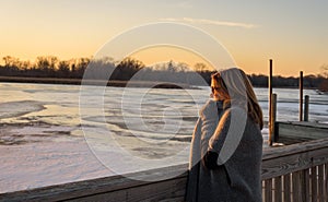 Woman standing on bridge over frozen river watching sunset