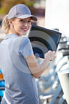 woman standing with city rent bicycle working with laptop