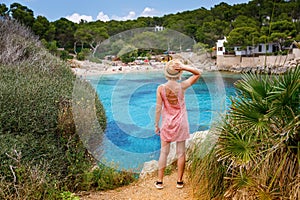 A woman standing on a cliff, enjoying the view of Cala Gat beach in Mallorca