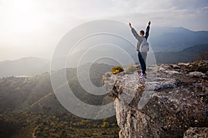 Woman standing on cliff with outstretched arms