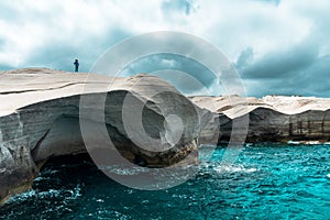 Woman standing on cliffs against the background of the cloudy sky. Sarakiniko. Milos Island, Greece.