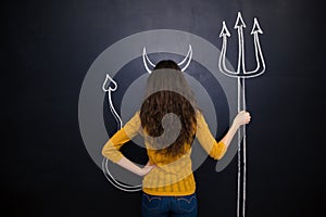 Woman standing with devils horns and trident drawn on blackboard