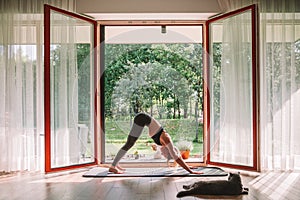 Woman standing in a Downward dog position in front of the opened window