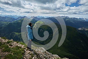 woman standing at the edge of a cliff overlooking high mountains. woman looking out over an idyllic mountain scene