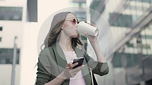 Woman standing in fall city street web surfing and drinking coffee