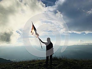 Woman standing with flag on the cliff mountain