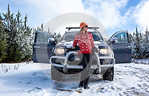 Woman standing in front of 4wd in snow among young pine forest