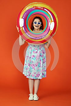 Woman standing in front of the camera looking through colorful inflatable tube smiling, isolated on orange background