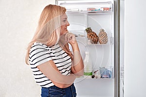 Woman is standing in front of the fridge and thinks what to eat