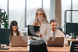 Woman is standing in front of her colleagues. Business people in formal clothes are working in the office together