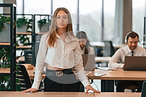 Woman is standing in front of her colleagues. Business people in formal clothes are working in the office together