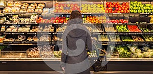 Woman standing in front of a row of produce in a grocery store.