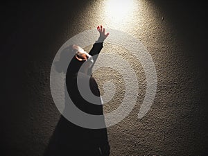 A woman standing with hand reaching the light in the dark.