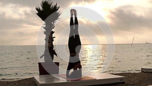 Woman standing on head in yoga pose salamba shirshasana outdoor, practicing yoga asana on the beach in front the sea