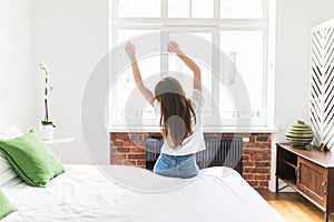 Woman standing in her bed near the window while stretching after waking up with sunrise at morning, back view