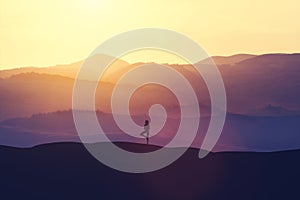 Woman standing on the hill, practicing yoga.