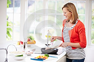 Woman Standing At Hob Preparing Meal In Kitchen