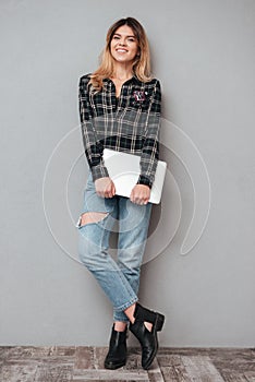 Woman standing and holding laptop over grey background