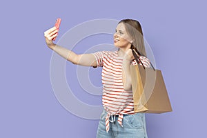 Woman standing holding shopping bag and making selfie or broadcasting livestream.