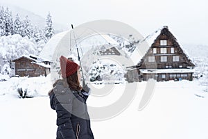 Woman standing and holding transparent umbrella in the winter and snow is falling at Shirakawago village, Japan.