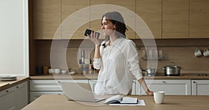 Woman standing in kitchen having conversation on cellphone using speakerphone