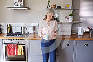 Woman Standing In Kitchen Sending Text Message On Phone