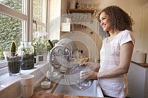 Woman Standing At Kitchen Sink Washing Up