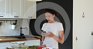 Woman standing in kitchen use smartphone search vegetarian recipes