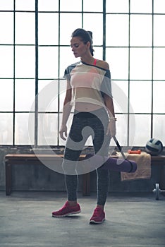 Woman standing in loft gym looking down holding yoga mat